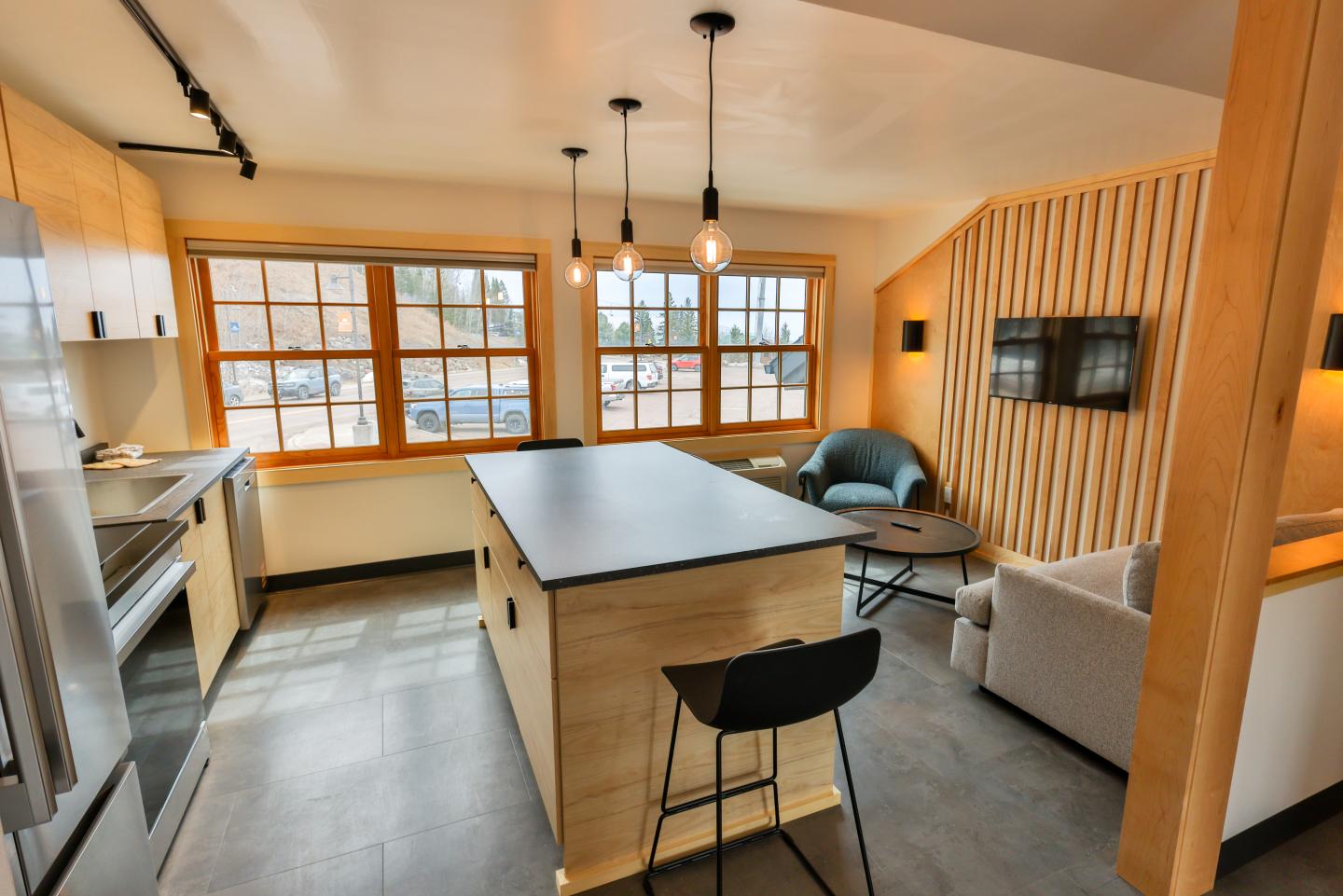 Modern kitchen and living area with wood accents and large windows.