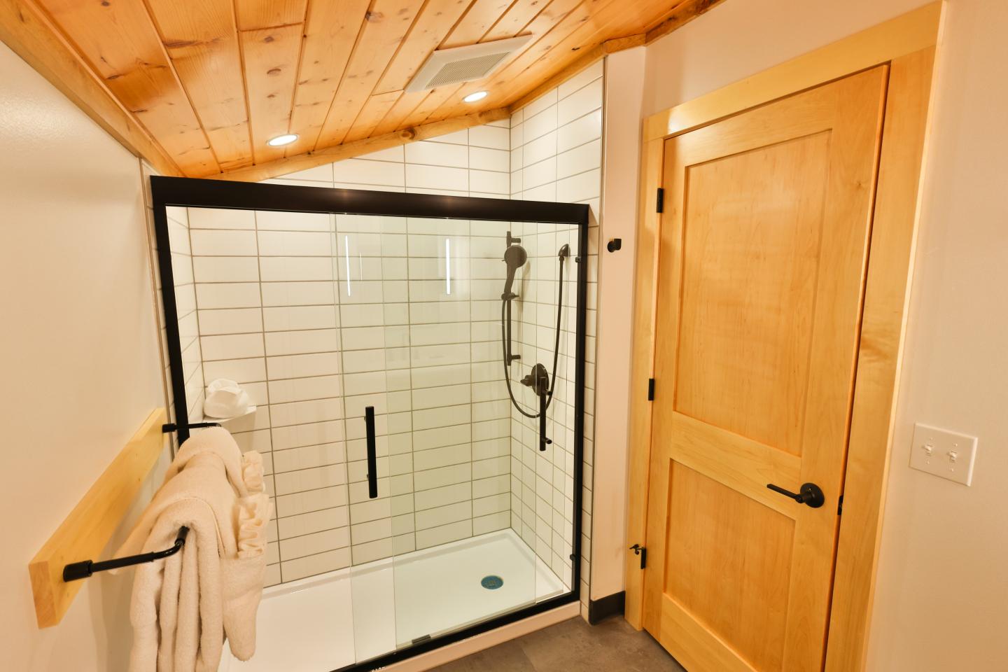 Shower with glass door, tiled walls, and a wooden ceiling.
