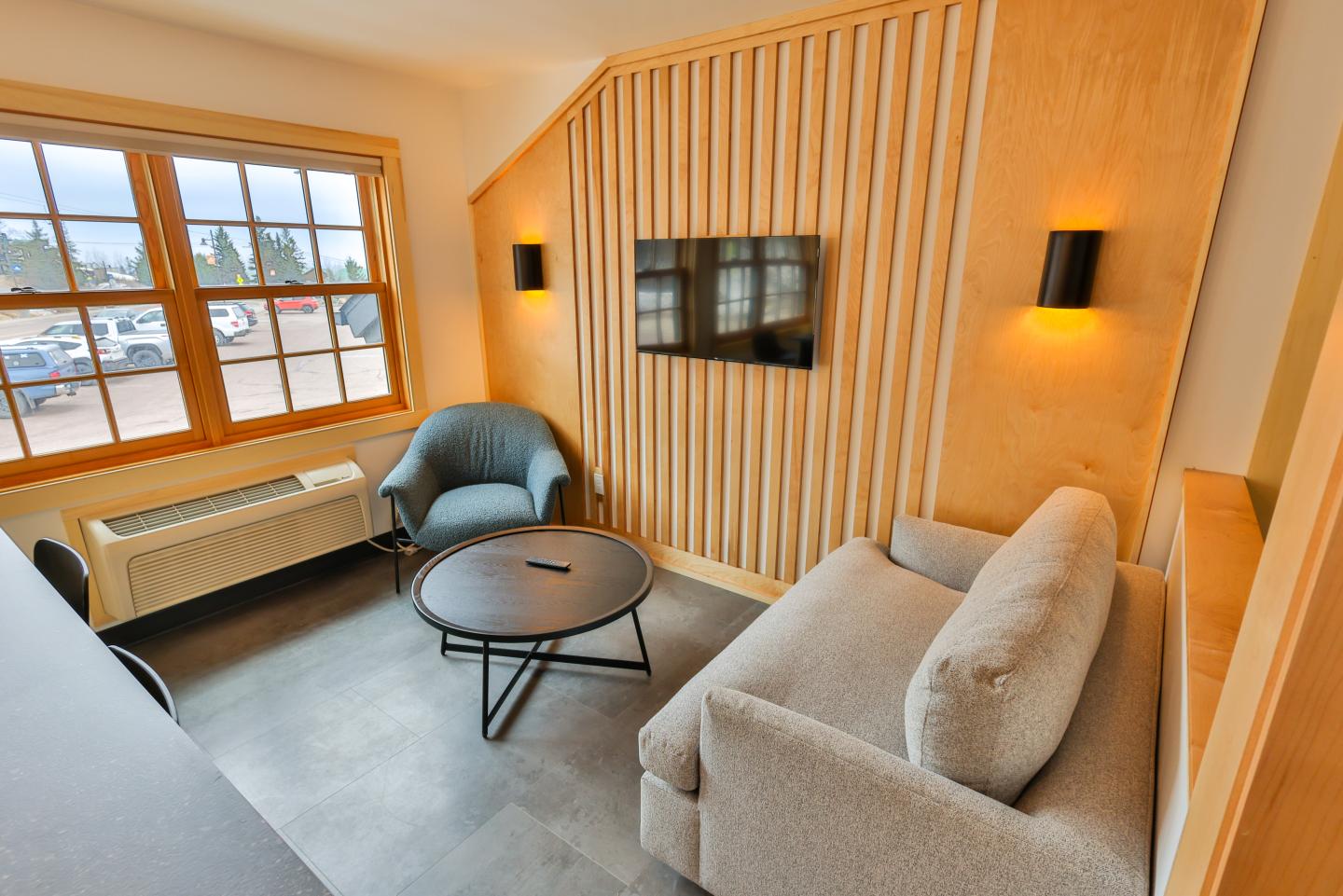 Cozy room with a sofa, armchair, round table, and TV on a wood-paneled wall.