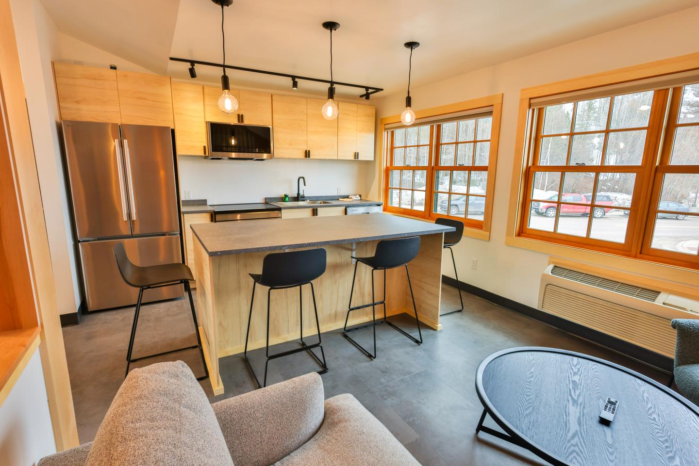 Modern kitchen with island, three chairs, pendant lights, large windows.