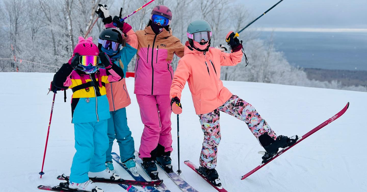 Four young skiers in colorful outfits pose joyfully on a snowy slope.