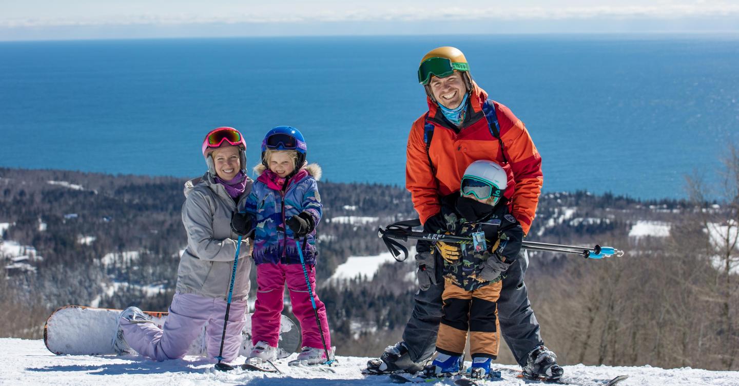Family skiing on a snowy hill with Lake Superior in the background.