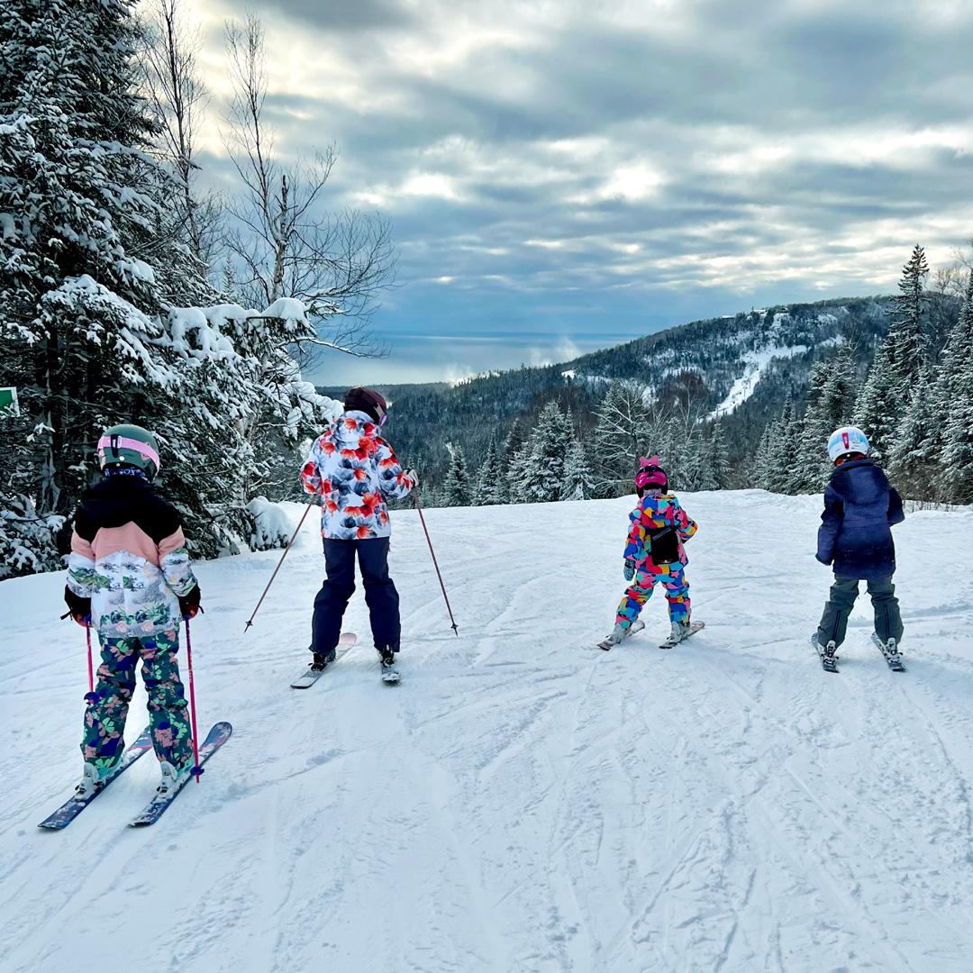 Four children skiing on a snowy mountain slope under a cloudy sky.