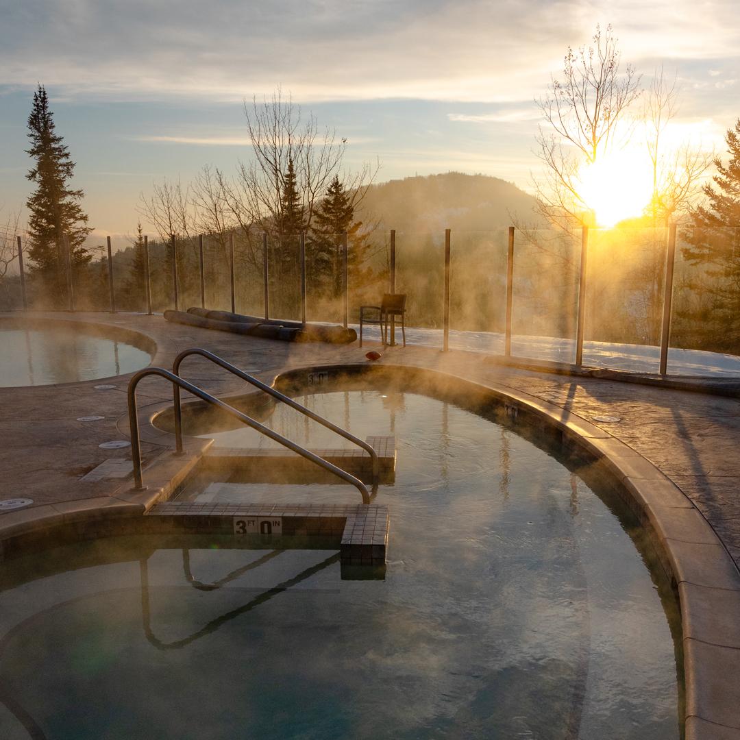 Steaming hot tub at sunrise with a mountain backdrop.