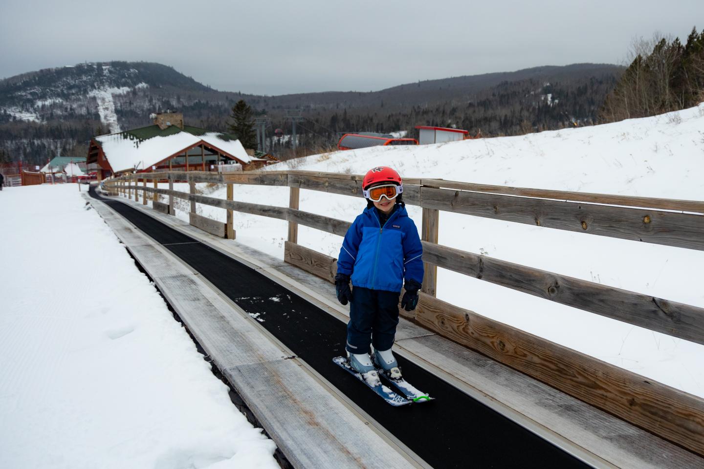 Child skiing on a conveyor belt in snowy mountains.