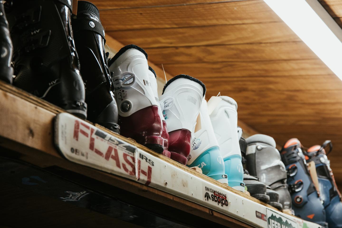 Ski boots lined up on a wooden shelf under warm lighting.