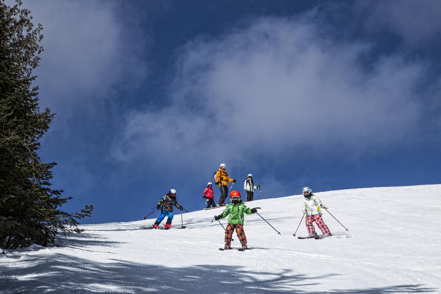 Skiers gliding down a snowy slope under a bright blue sky with clouds.