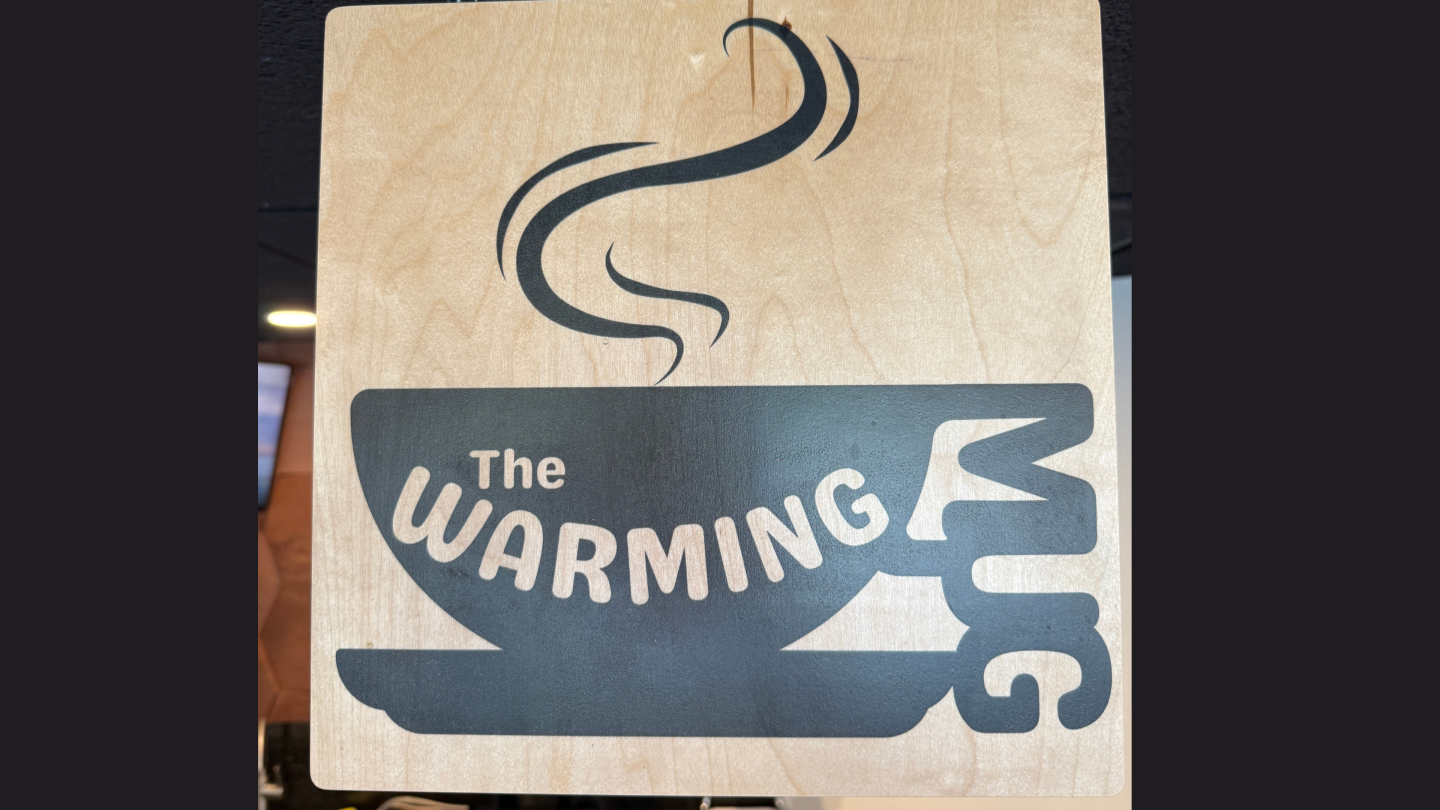 Wooden sign with a steaming coffee cup logo labeled "The Warming Mug."