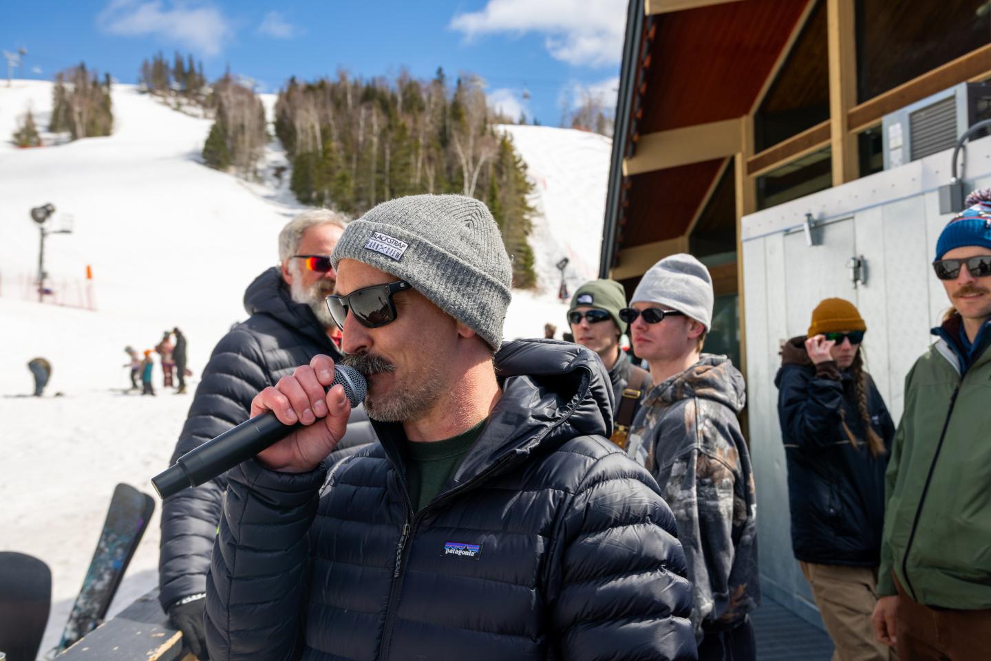 Man speaking into a microphone outdoors at a snowy ski resort.