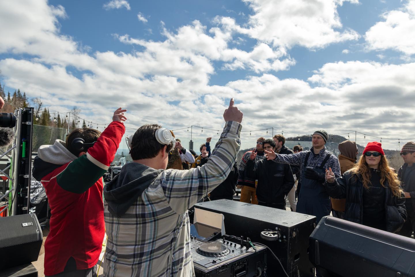 DJ performs for a cheering outdoor crowd under a cloudy sky.