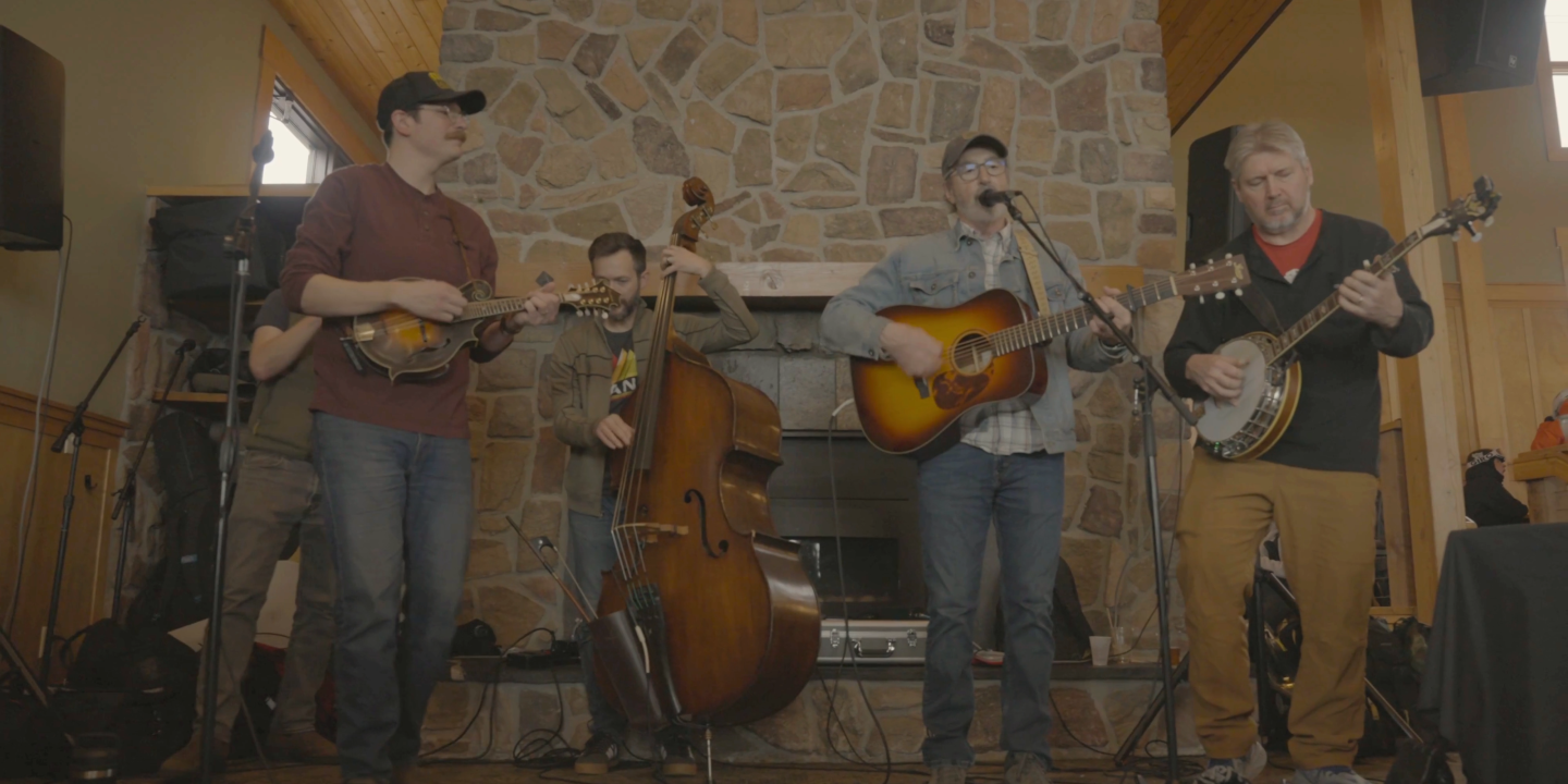 Three musicians perform with guitars and upright bass in a rustic stone-walled room.