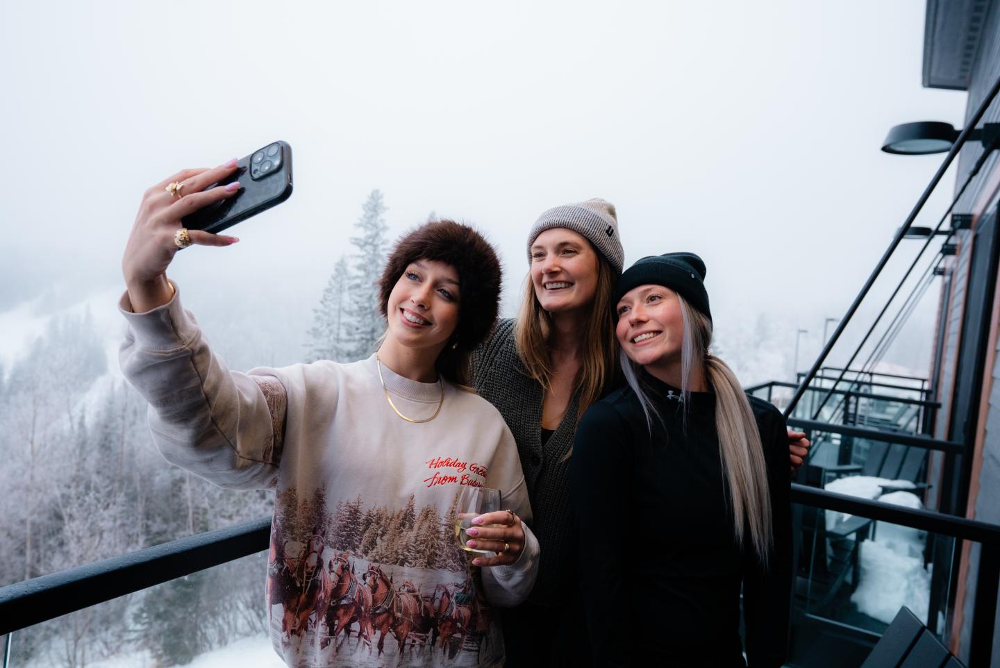 Three women taking a selfie on a snowy balcony.