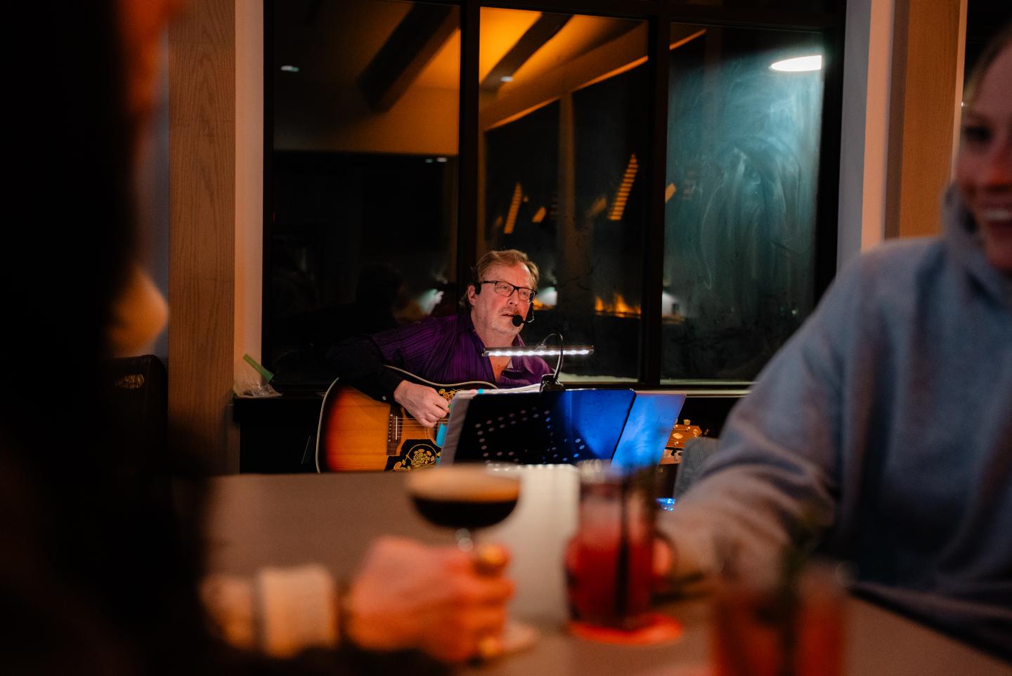 Man plays guitar and sings in a warmly lit restaurant as diners sit in the foreground.