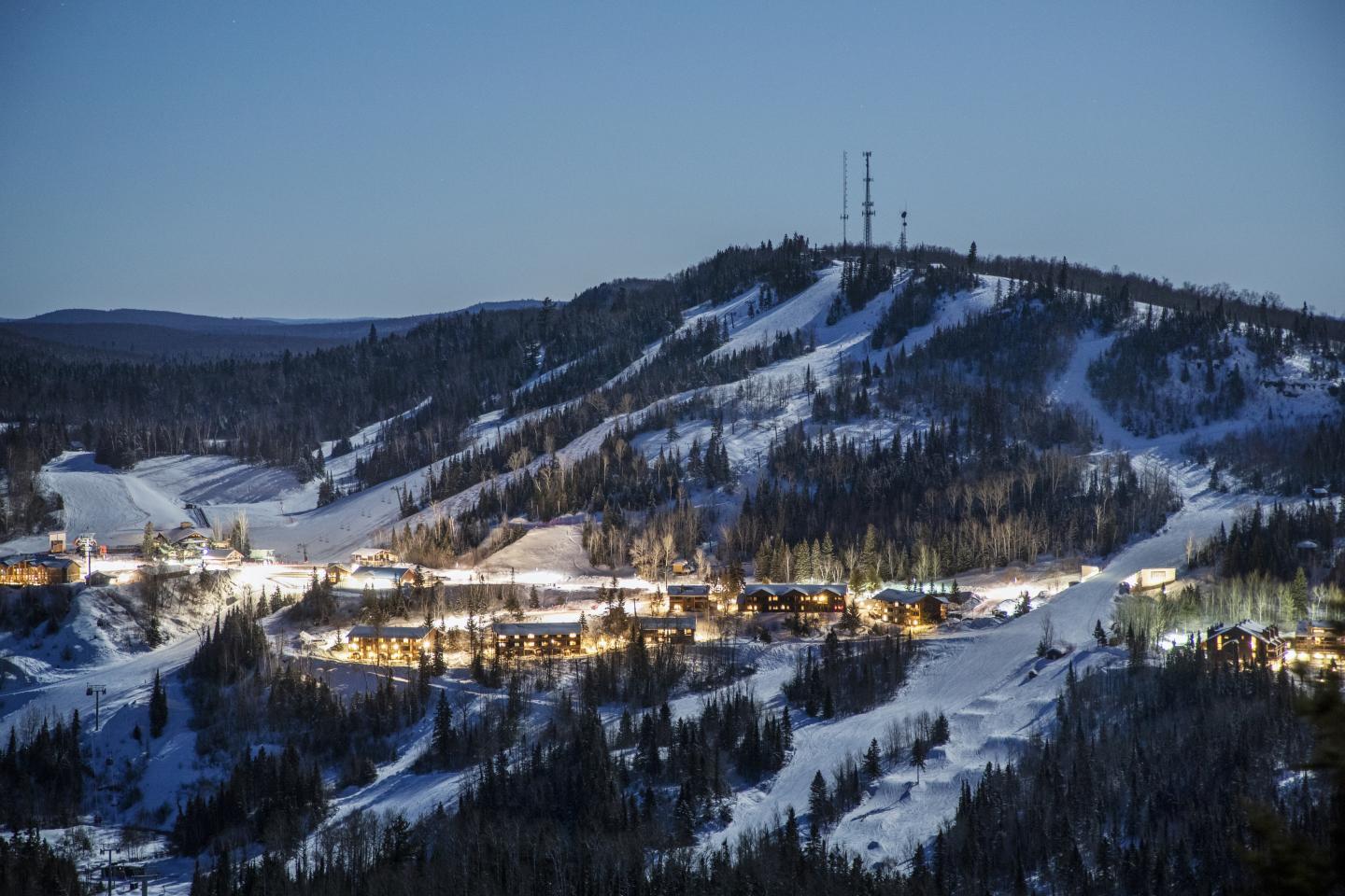 Snow-covered ski resort village glowing at dusk beneath forested hills.