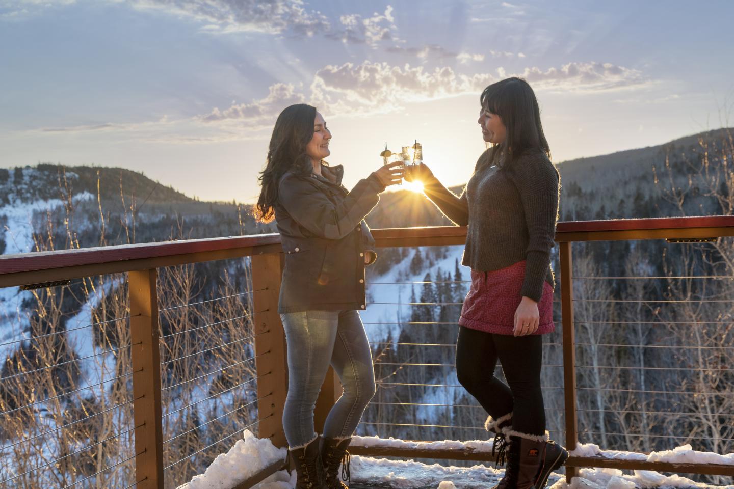 Two women clinking glasses at sunset