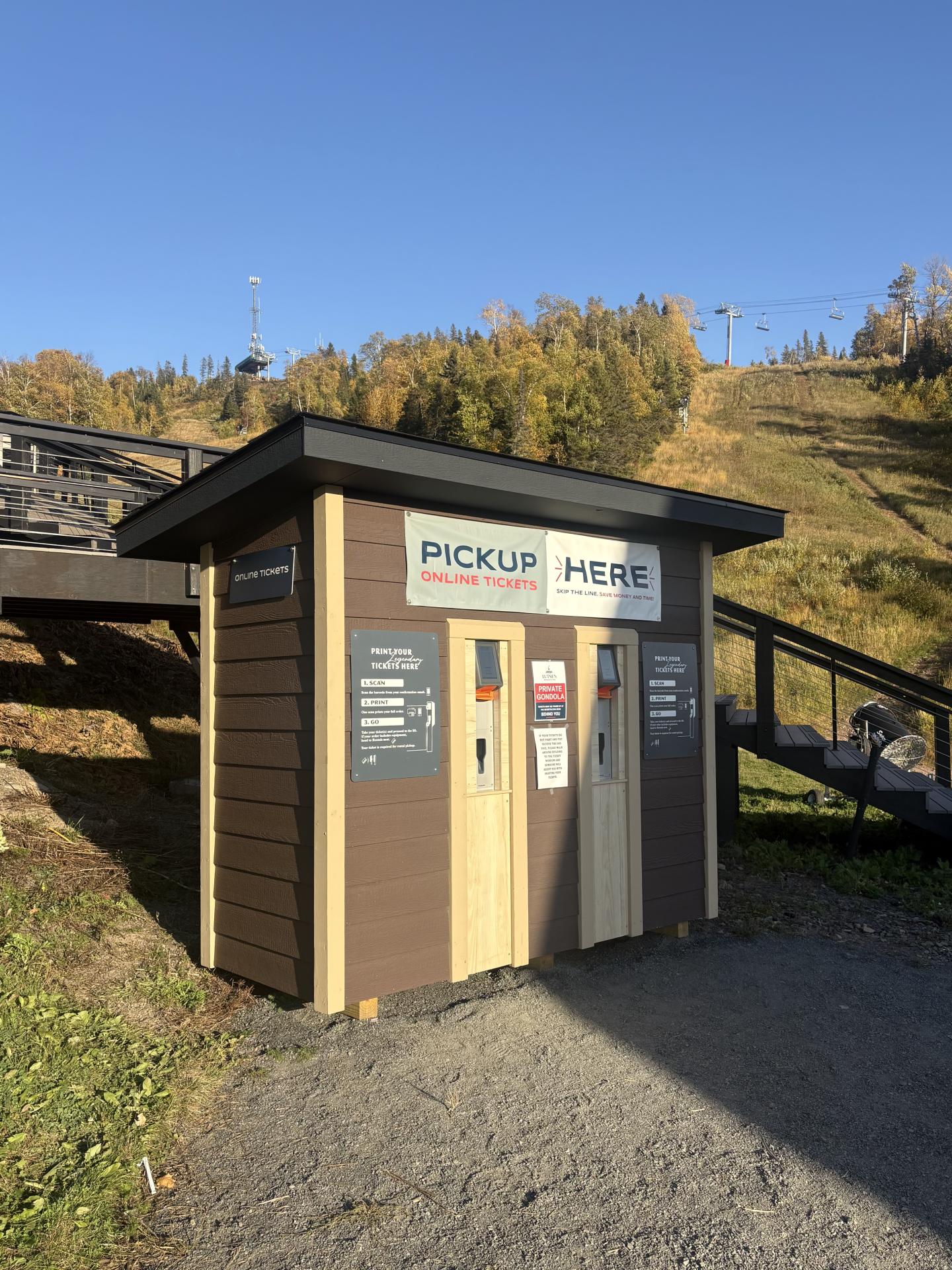 Small outdoor pickup box with beige and dark gray lockers beside a hillside.